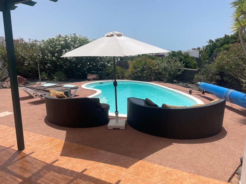 A pool area with a white umbrella, two black lounge chairs, and a blue water slide.