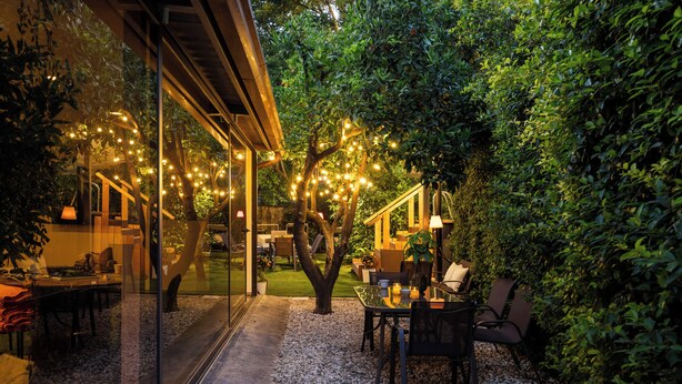 Un patio al aire libre con pared de vidrio, una mesa con sillas y luces colgantes.