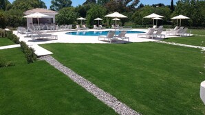 Piscina con sillas de descanso y sombrillas, rodeada de césped cuidado y árboles.