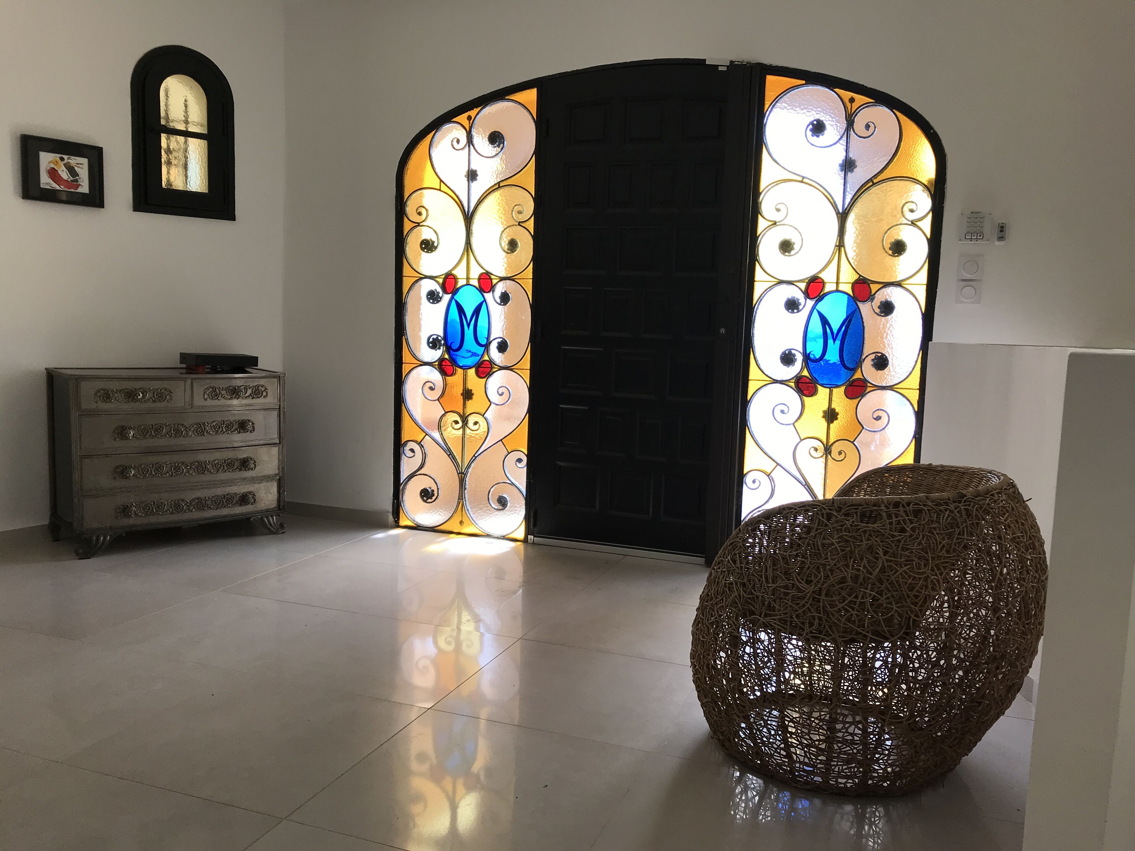 A room with a large black door, a wicker chair, a dresser, and a framed picture on the wall.