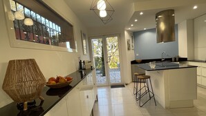 A modern kitchen with a large island, a dining area with stools, and a view of the outdoors through a glass door. - AGAY - Charming villa with heated swimming pool and exceptional sea view (Saint-Raphaël)
