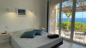 A bedroom with a bed, pillows, a bedside table, a lamp, a framed picture, and a view of the sea through large windows. - AGAY - Charming villa with heated swimming pool and exceptional sea view (Saint-Raphaël)