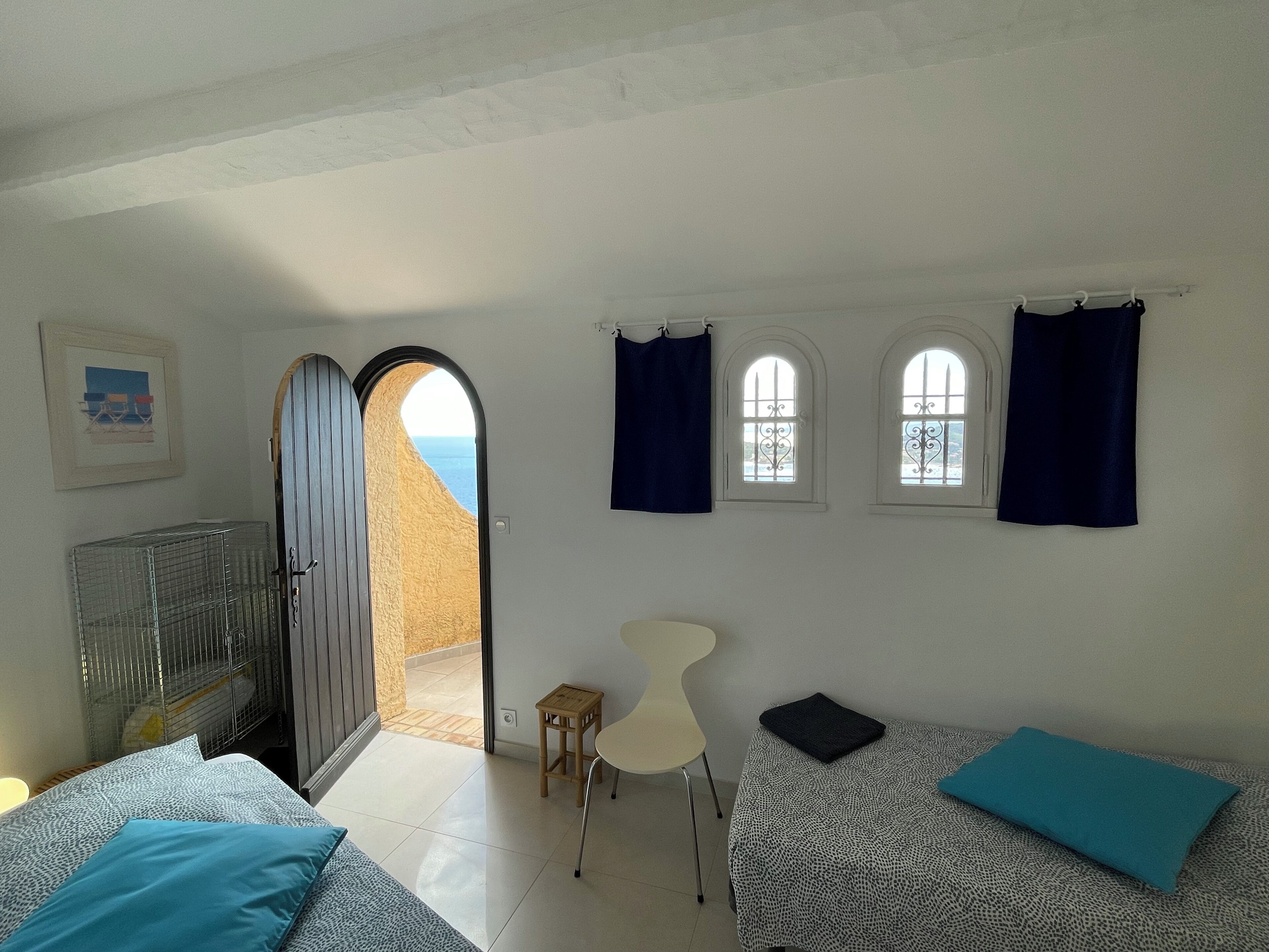 A room with a bed, a desk, and a view of the sea through an arched doorway.