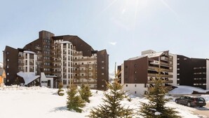 A modern multi-story building with a mix of brown and white exterior panels, surrounded by snow and evergreen trees. - apartment/ flat - Alpe d'huez (Huez)