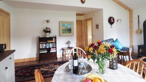 Zona pranzo con tavolo apparecchiato per due, una libreria, un'esposizione floreale e un soffitto rustico con una testa di cervo.