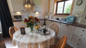 Cucina accogliente con tavolo da pranzo per due, adornata da un centrotavola floreale, una bottiglia di vino e una macchina per il pane.
