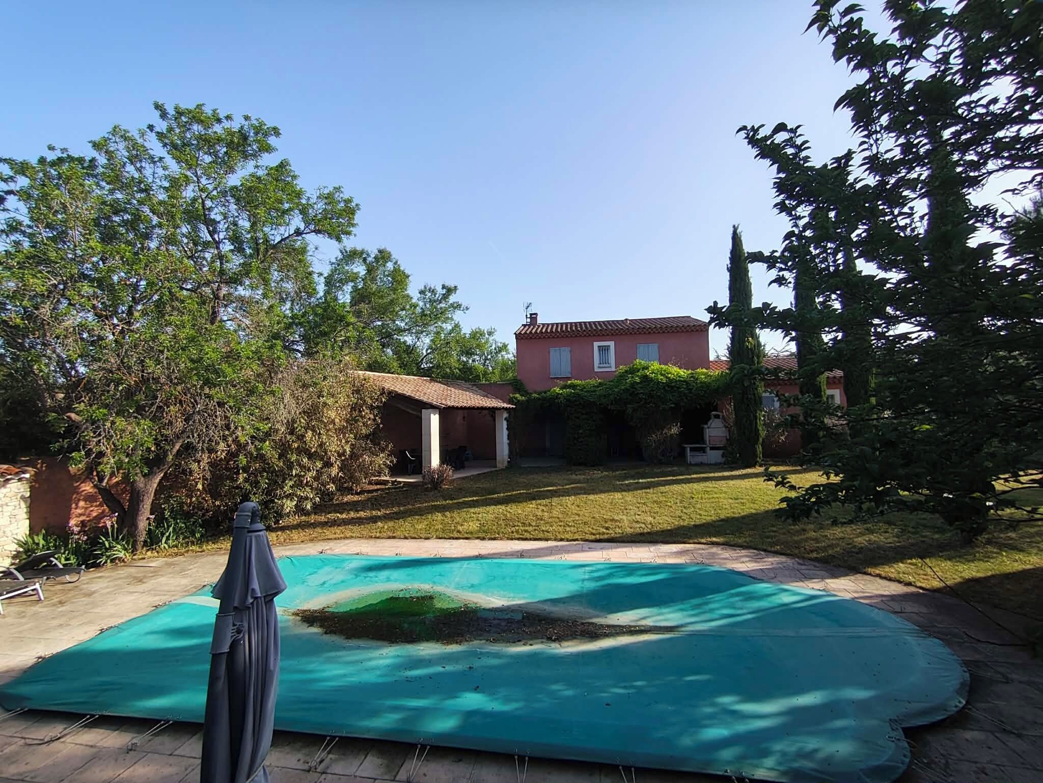 A backyard with a swimming pool, a covered patio, and a house in the background.