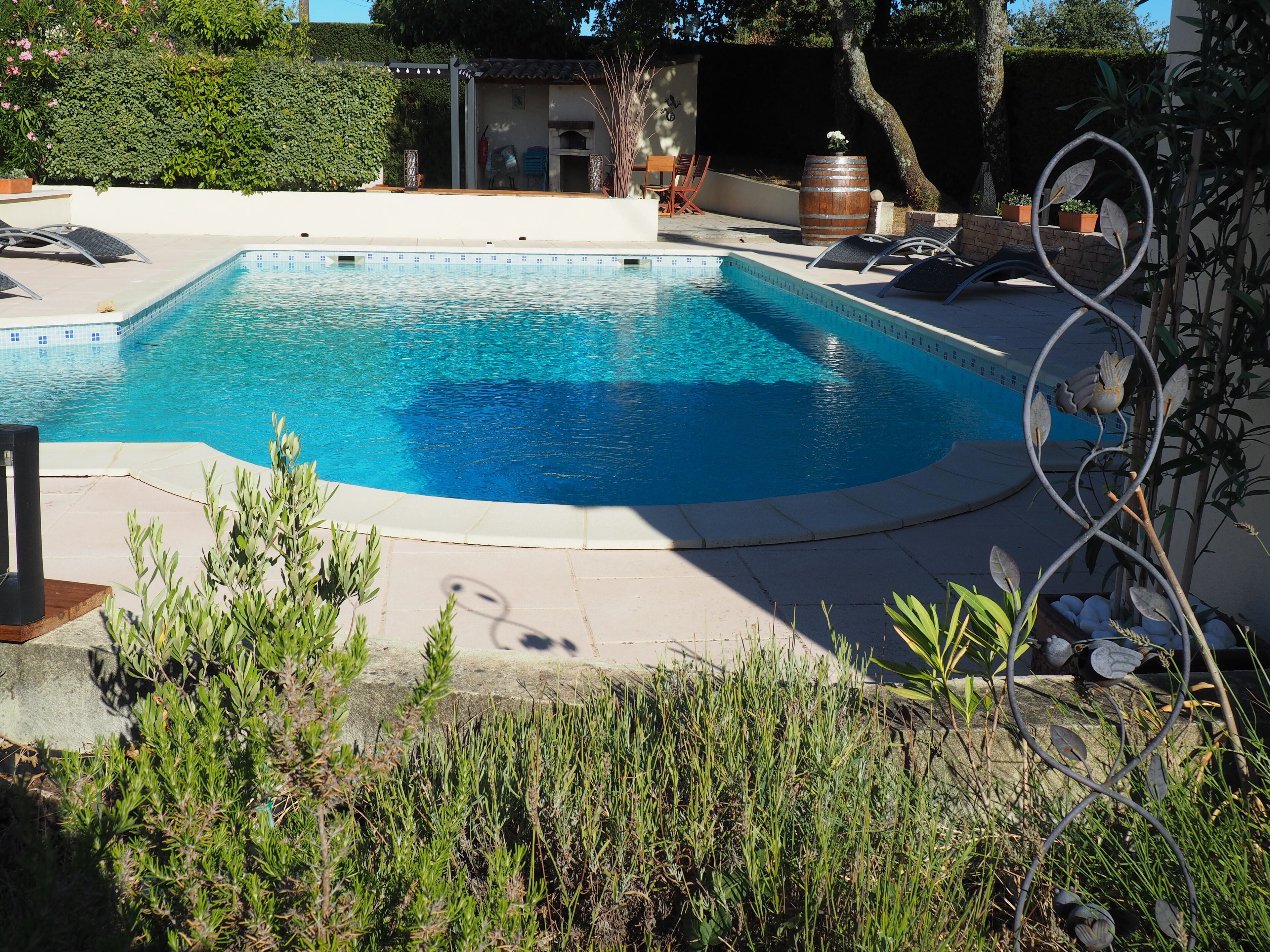 Una piscina de vora corba, envoltada per una zona de terrassa amb gandules i un barbacoa.