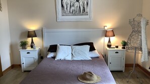 Een keurig opgemaakte slaapkamer met een groot bed, twee nachtkastjes met lampen, een kunstwerk in een lijst erboven, en een vloerlamp aan de rechterkant.