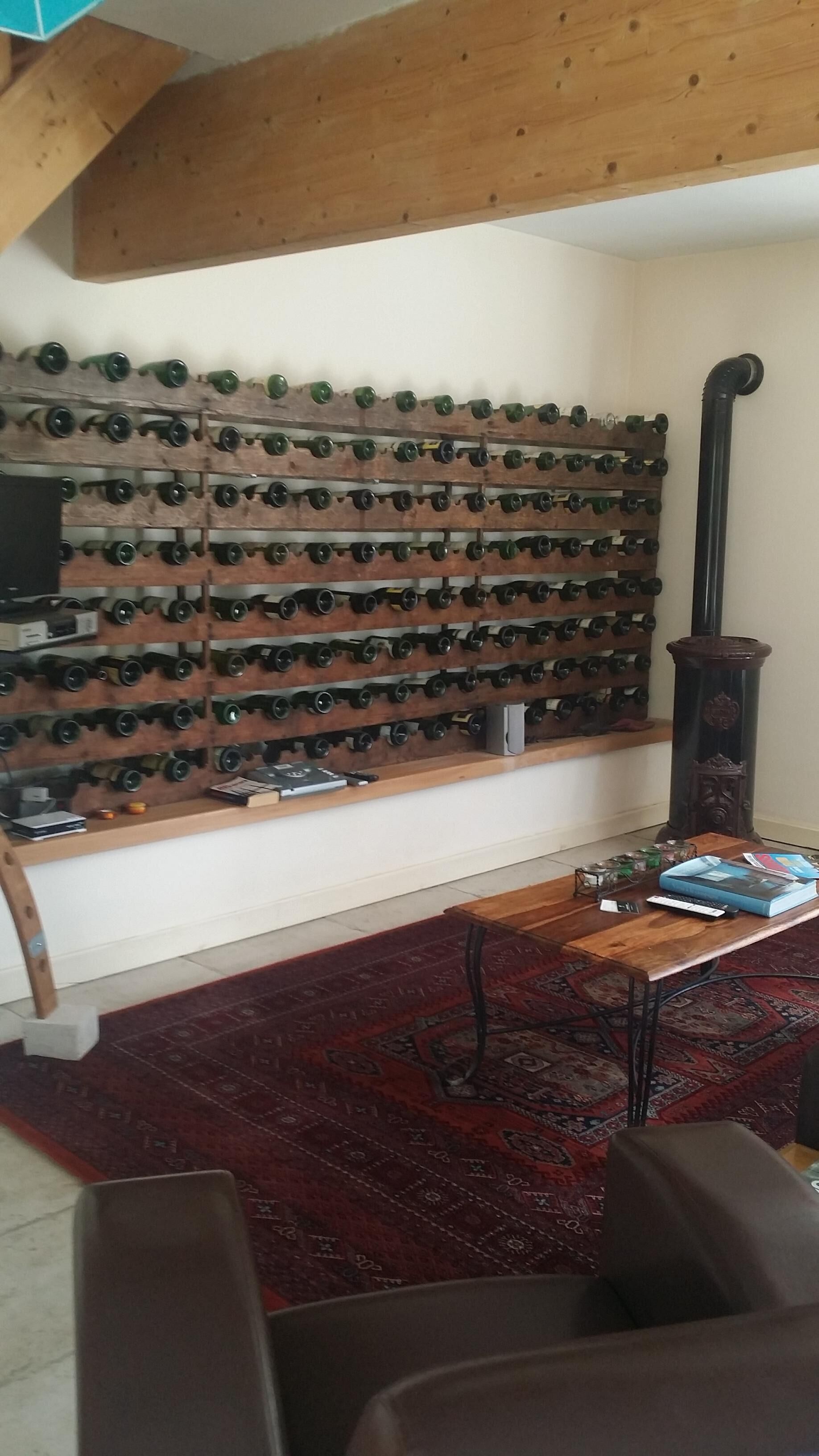 A room with a wall-mounted wine rack, a wooden table with a book and remote control, and a patterned rug.