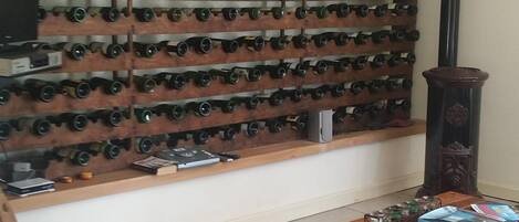 A room with a wall-mounted wine rack, a wooden table with a book and remote control, and a patterned rug.
