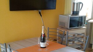 A dining area with a table, chairs, a bottle of champagne, and a television mounted on the wall. - Lauretta apartment in elegant complex (Ceriale)