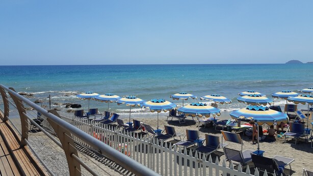 A beach with rows of blue and white umbrellas, beach chairs, and a wooden deck with a railing. - Lauretta apartment in elegant complex (Ceriale)