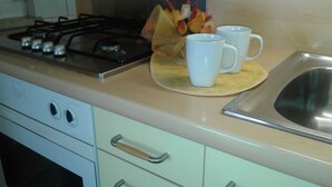 A kitchen with a gas stove, a sink, and a dish rack with cups and a strainer. - Lauretta apartment in elegant complex (Ceriale)