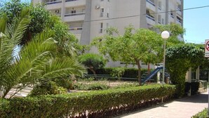 Un edificio moderno de varios pisos con balcones, rodeado de vegetación cuidada y un cielo despejado.