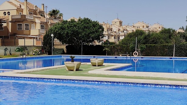 Una piscina con borde de azulejos, rodeada de césped y algunas sillas de descanso.