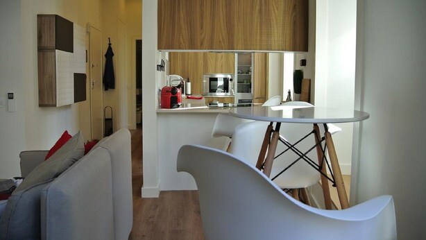 Una cocina moderna con armarios blancos, un hervidor rojo y una mesa de cristal.