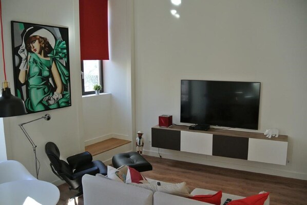 Una sala de estar moderna con un televisor de pantalla plana sobre un mueble blanco y negro, un cuadro en la pared y una persiana roja en la ventana.