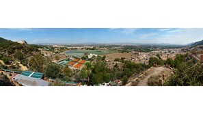 Panoramic view of a hilltop structure overlooking a town with a sports facility or public park below.
