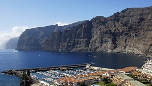 A coastal marina with boats docked, a rocky cliff in the background, and a building with a red roof in the foreground. - APARTMENT WITH SEA VIEWS AND FANTASTIC SUNSHINE (Santiago del Teide)