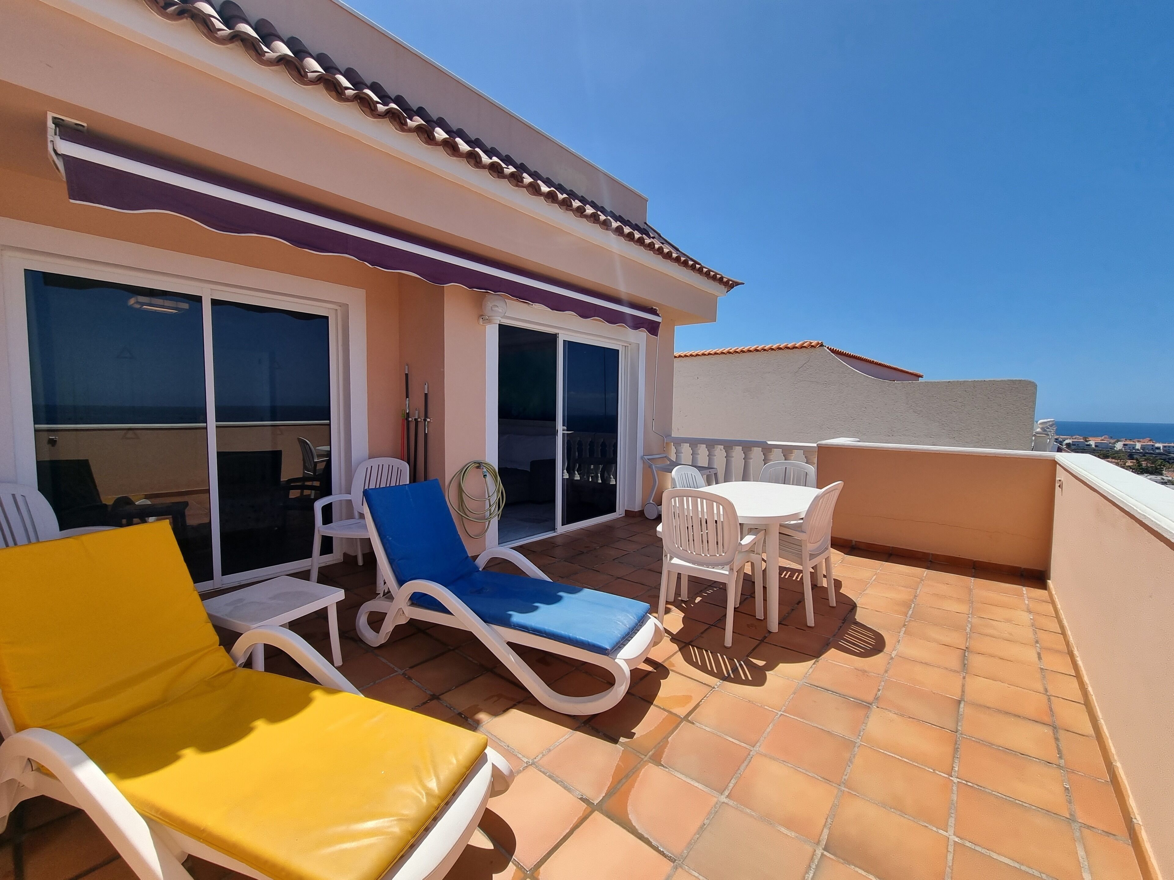 Une terrasse avec des fauteuils de jardin blancs et une table, une porte-fenêtre coulissante et une vue sur la mer.