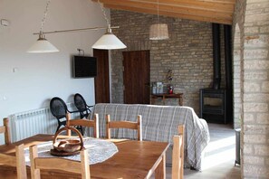 A cozy dining area with a wooden table and chairs, a television, and a stone wall with a fireplace.
