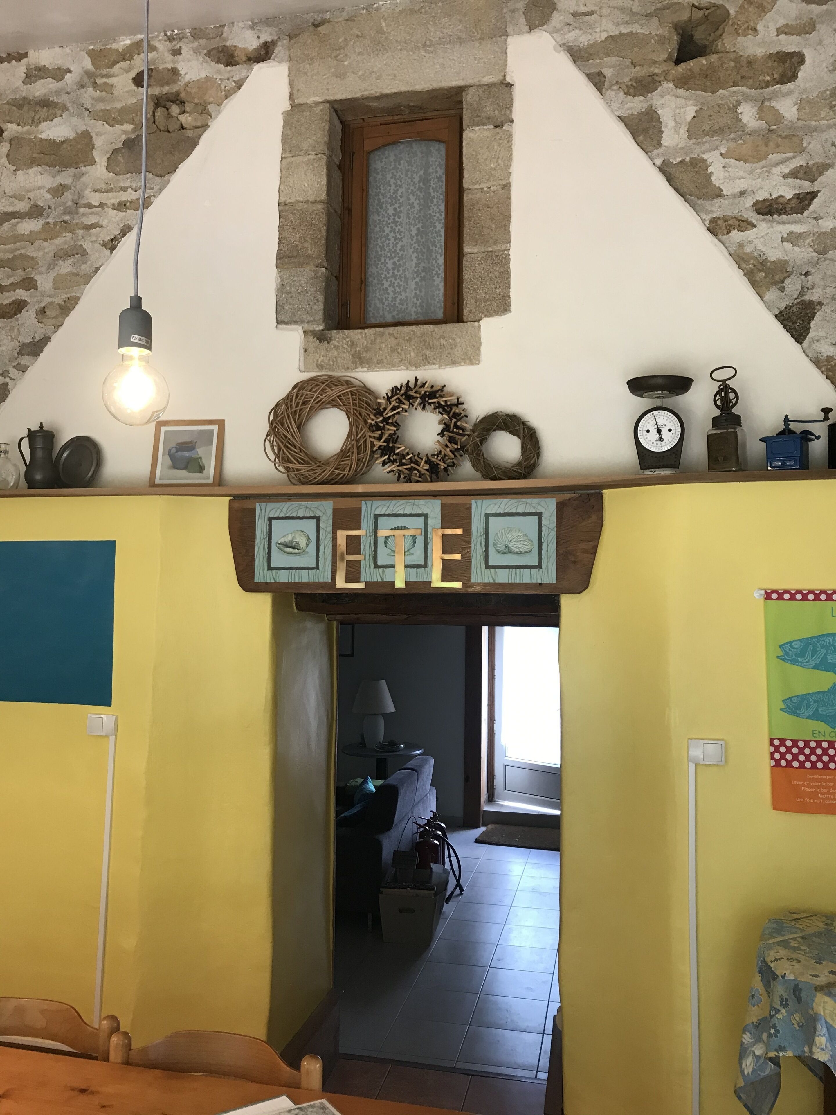 Un intérieur rustique avec un mur en pierre, un plafond en bois et un mur jaune orné d’une inscription « ETE ».