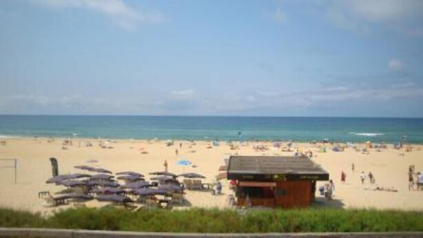 A beach with umbrellas and a small building, likely a beach hut or snack bar.
