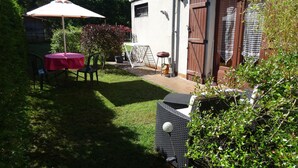 A patio with a table and chairs, a grill, and a white fence.