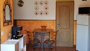 A compact kitchen with a dining table, chairs, a coffee machine, a refrigerator, a clock, and a decorative wall piece.