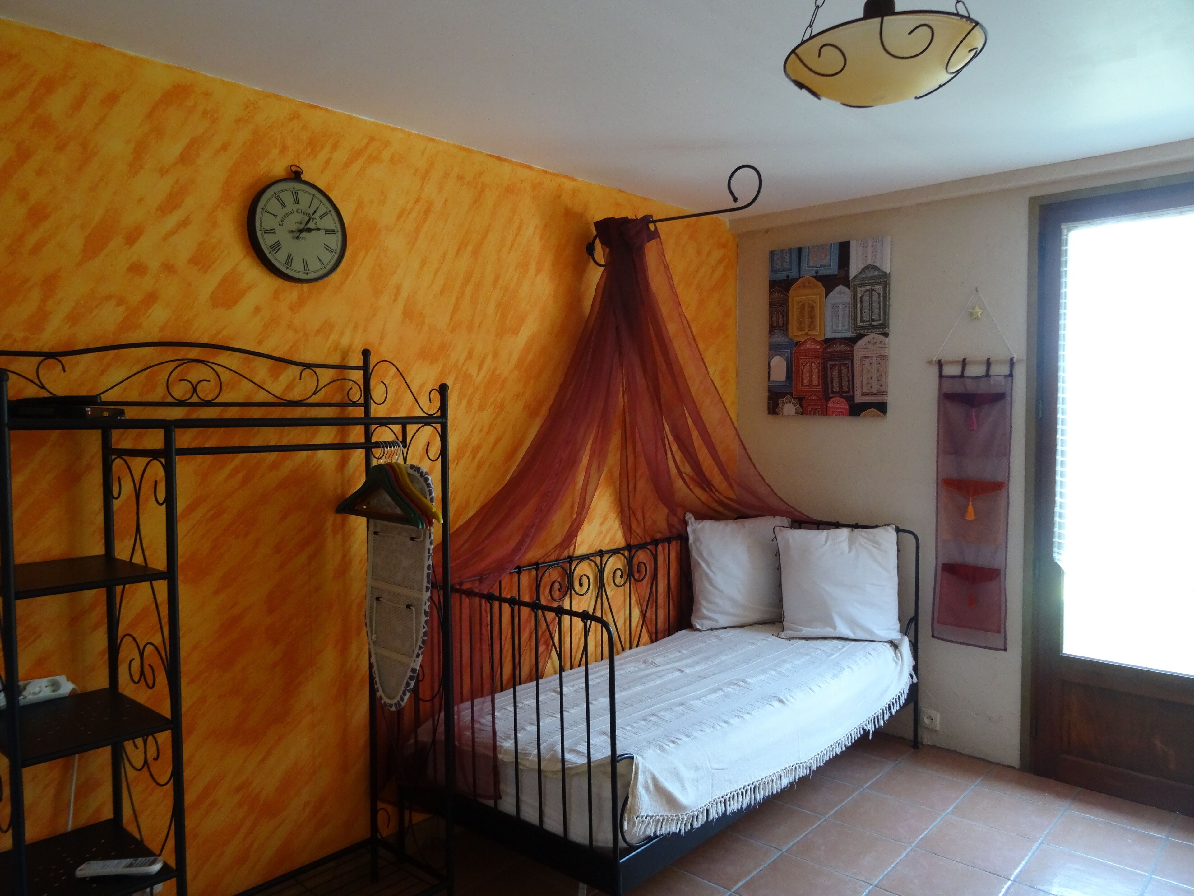 Ein Zimmer mit Bett, einer Uhr, einem Regal und einem Fenster.