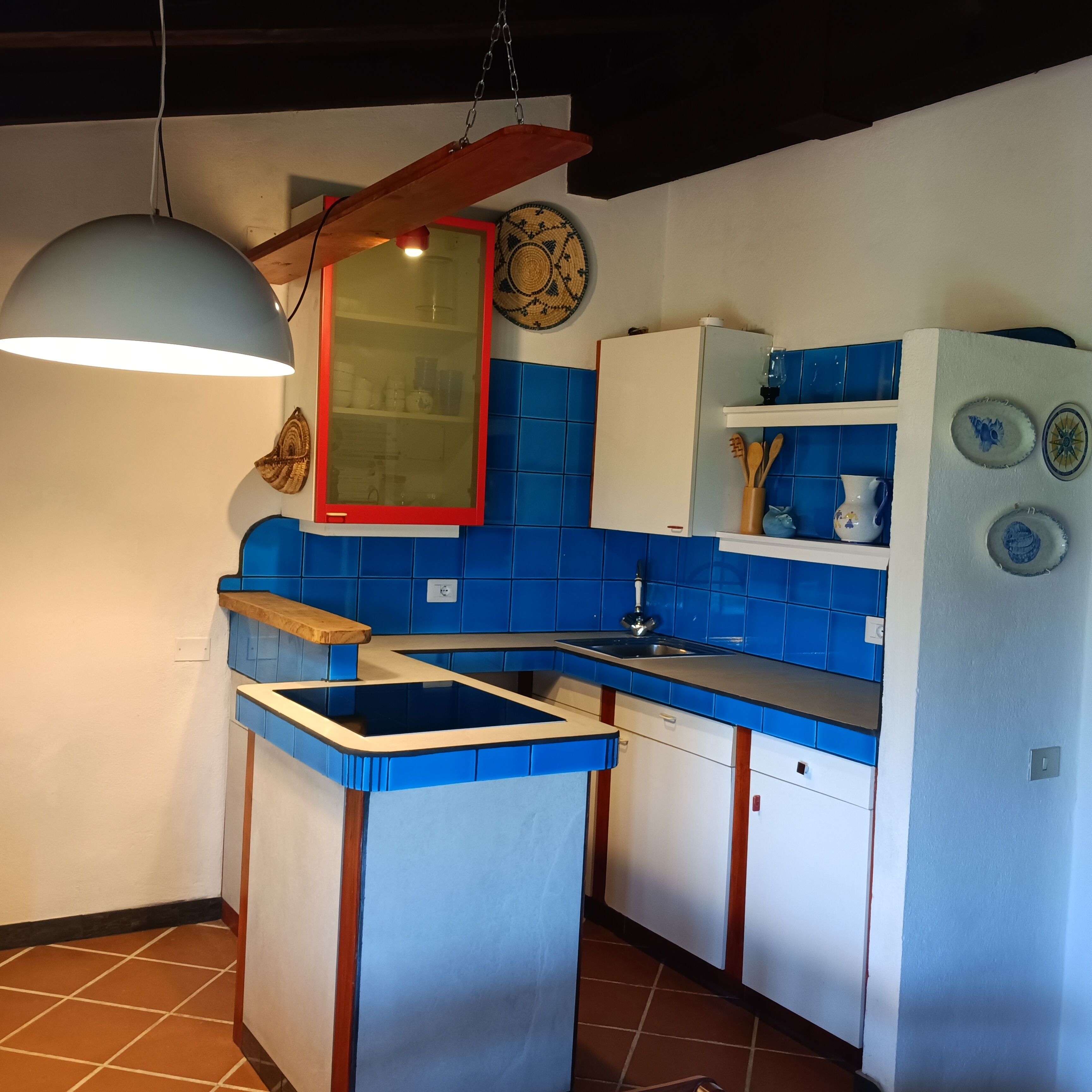 Uma cozinha compacta com azulejos azuis, bancada de madeira, luminária pendente e geladeira.