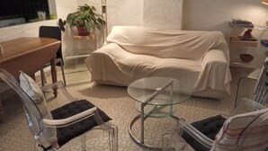 Un salon comprenant un canapé, une table en verre, une table à manger, des chaises, une plante en pot et une lampe.
