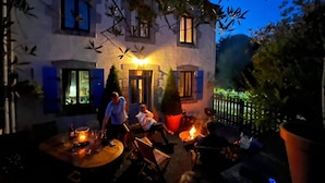 An outdoor seating area with a fire pit, a table with candles, and a building with blue shutters.