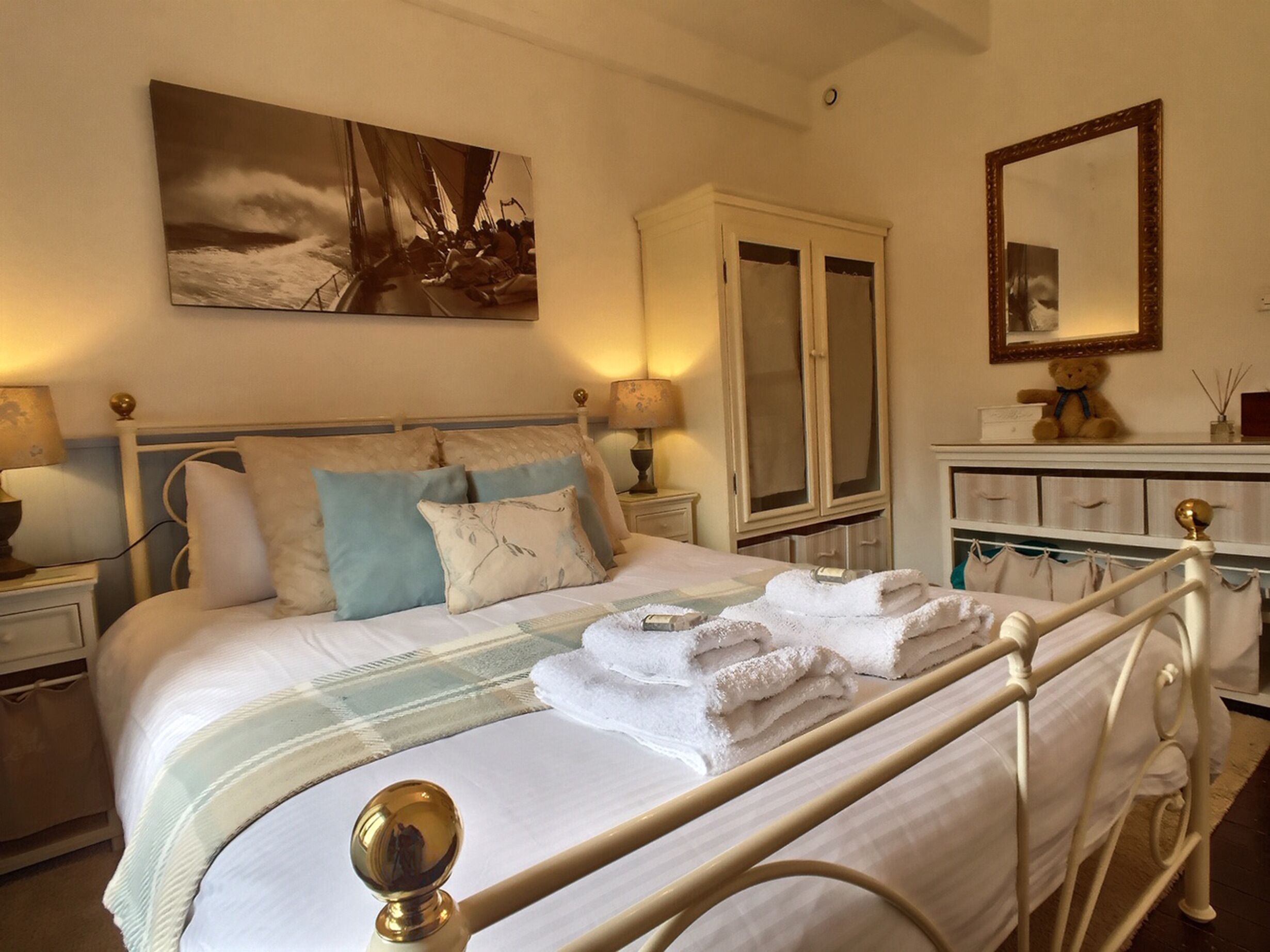 A neatly made bed with a headboard, a bedside table with a lamp, a wardrobe, and a mirror on the wall.