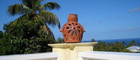 A terracotta pot on a white pedestal with a railing, palm trees, and a clear blue sky in the background.