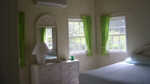 A bedroom with a bed, a dresser, a mirror, and two windows with curtains. - Villa with large pool, screened terrace overlooking Caribbean. (Jessops)