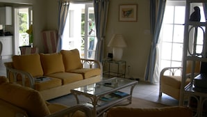A living room with a yellow sofa, a glass coffee table, wicker chairs, and a lamp. - Villa with large pool, screened terrace overlooking Caribbean. (Jessops)