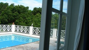 A view of a swimming pool with a white fence, a bird on the fence, and a patio area with a table and chairs. - Villa with large pool, screened terrace overlooking Caribbean. (Jessops)