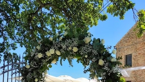 An outdoor wedding arch with white flowers and greenery, set against a clear sky.