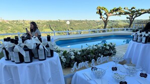 A poolside setting with tables set for a wedding reception, featuring bottles of wine and a floral arrangement.