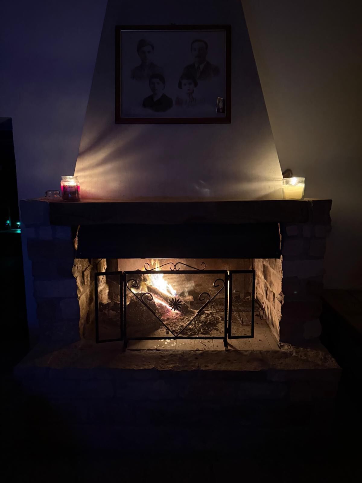 A fireplace with a framed picture above it, a candle on the mantel, and a lit fire below.