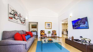 A living room with a grey sofa, red and blue cushions, a glass coffee table, and a TV on the wall. - Villa Qura - Three Bedroom Villa, Sleeps 6 (Montaña Roja)