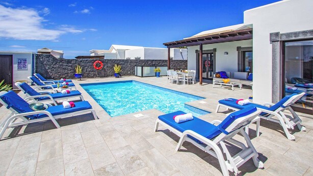 A swimming pool with lounge chairs and a stone wall. - Villa Qura - Three Bedroom Villa, Sleeps 6 (Montaña Roja)