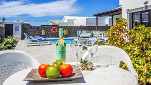 A poolside area with lounge chairs, a table with fruit and a bottle, and a view of the sea. - Villa Qura - Three Bedroom Villa, Sleeps 6 (Montaña Roja)