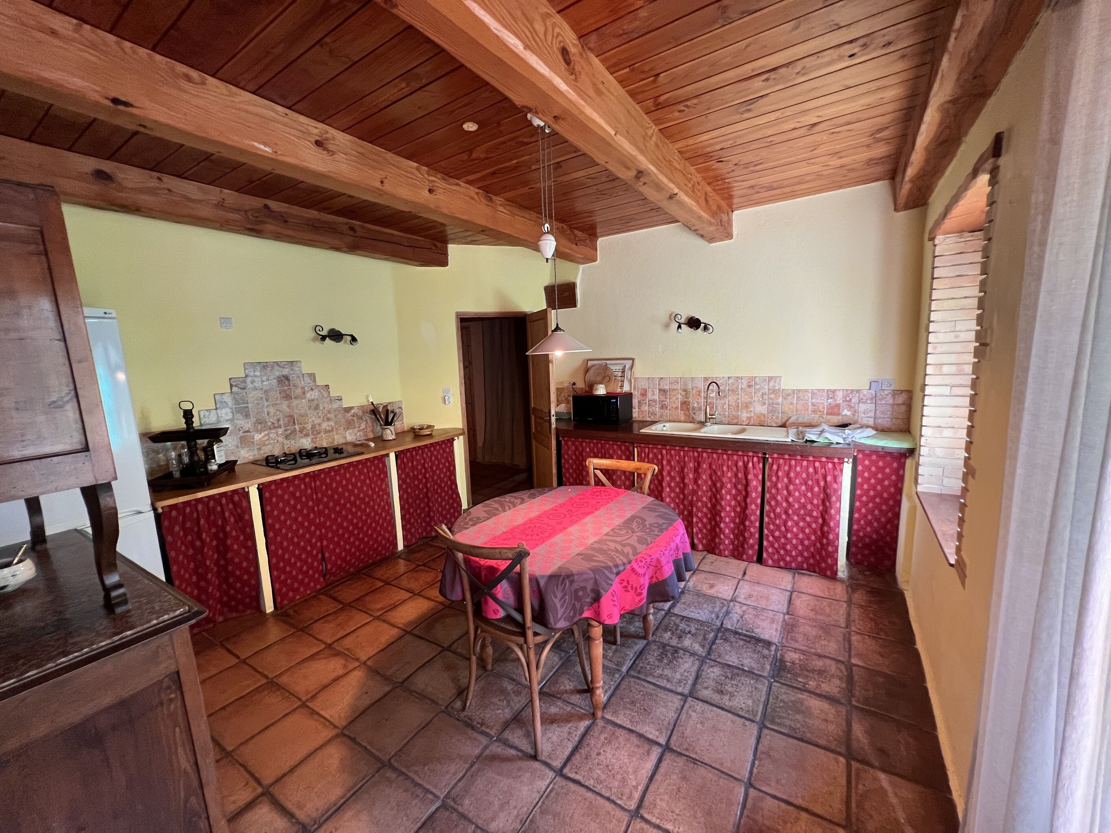 A compact kitchen with a dining area, wooden ceiling beams, and a tiled floor.