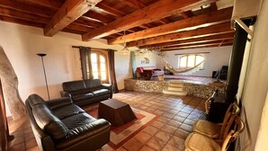 A spacious living area with a stone fireplace, a black leather sofa, a wooden chair, and a piano. - For Nature Lovers ... (Saint-André-D'olérargues)