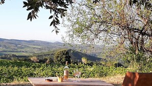 A wooden table with a bottle and glasses, set outdoors with a vineyard and hills in the background. - For Nature Lovers ... (Saint-André-D'olérargues)