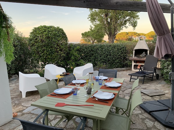 Een terras met een eettafel gedekt voor twee personen, omringd door stoelen, een barbecue en een pergola.