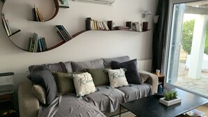 Una sala moderna con un sofá gris, una estantería redonda y una ventana con vistas a zonas verdes.
